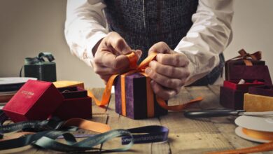 Craft Boxes - A person wraps a gift with orange ribbon on a rustic wooden table, surrounded by boxes.