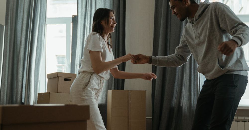 Home Goods Boxes - Happy couple dancing among cardboard boxes in their new home, celebrating a fresh start.