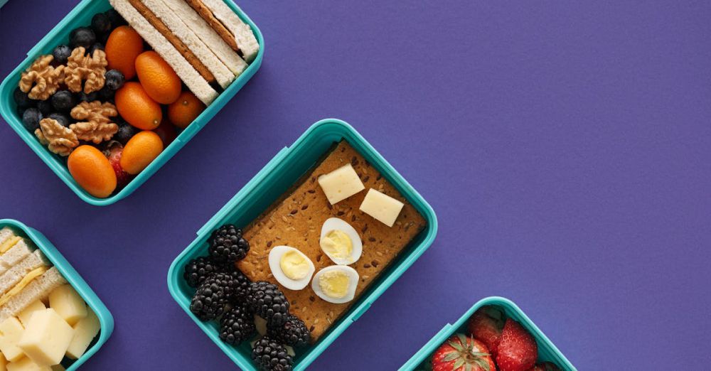 Snack Boxes - Flat lay of diverse snacks in plastic containers on a purple background.