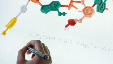 Science Kits - Anonymous chemist writing with marker on illuminated magnetic board formula of Hydronium and Acetate production after studying plastic model of molecule in laboratory