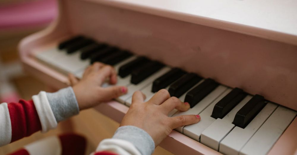 Musical Toys - Close-up of child's hands playing a pink toy piano indoors.