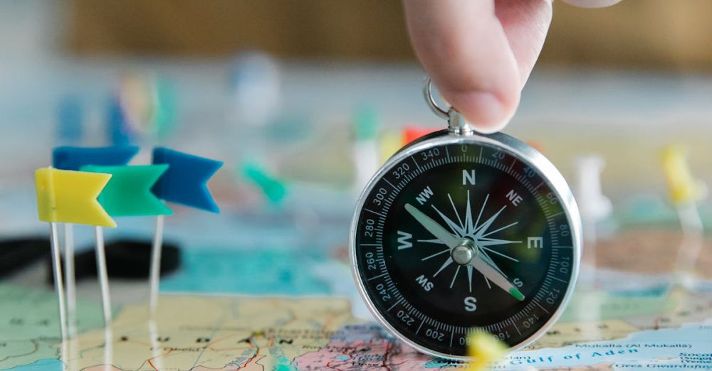 Geography Tools - Close-up of hand holding compass over a map with colorful pins and flags, symbolizing travel planning.