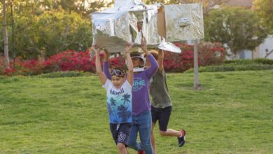 Science Games - Children joyfully playing with a homemade cardboard rocket outdoors on a sunny day.