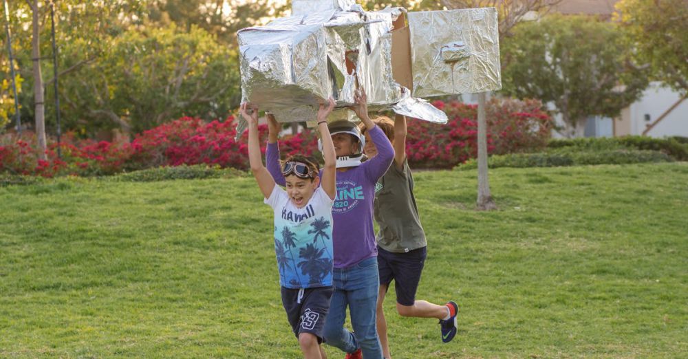 Science Games - Children joyfully playing with a homemade cardboard rocket outdoors on a sunny day.