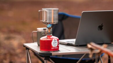 Camping Stoves - A cozy outdoor workstation featuring a laptop and portable stove on a foldable table amidst nature.