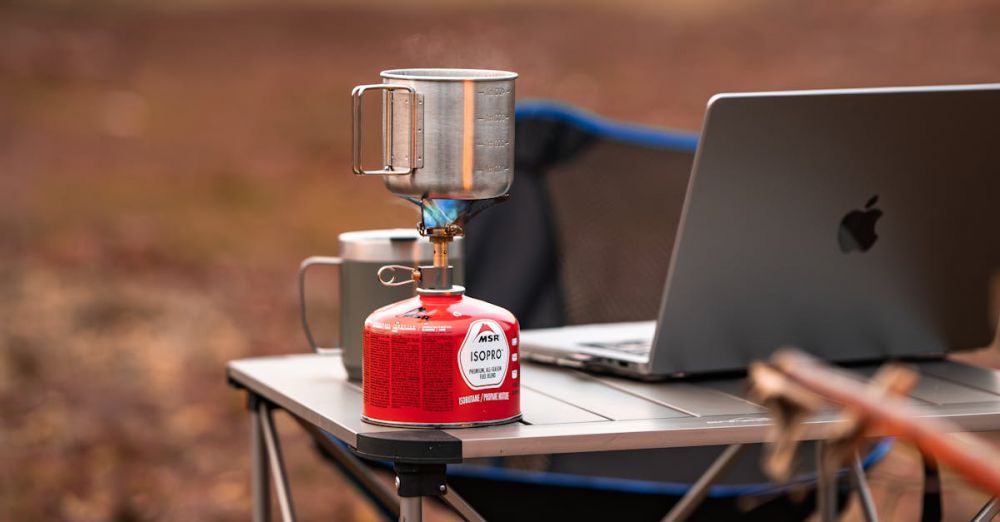 Camping Stoves - A cozy outdoor workstation featuring a laptop and portable stove on a foldable table amidst nature.