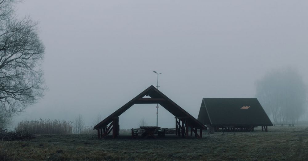 Camping Tables - A foggy morning at a tranquil picnic site with two wooden gazebos amidst a grassy field.