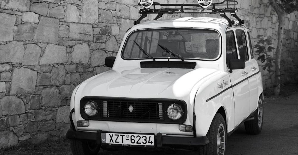 Headlamps - Classic white Renault car parked by a rustic stone wall outdoors.