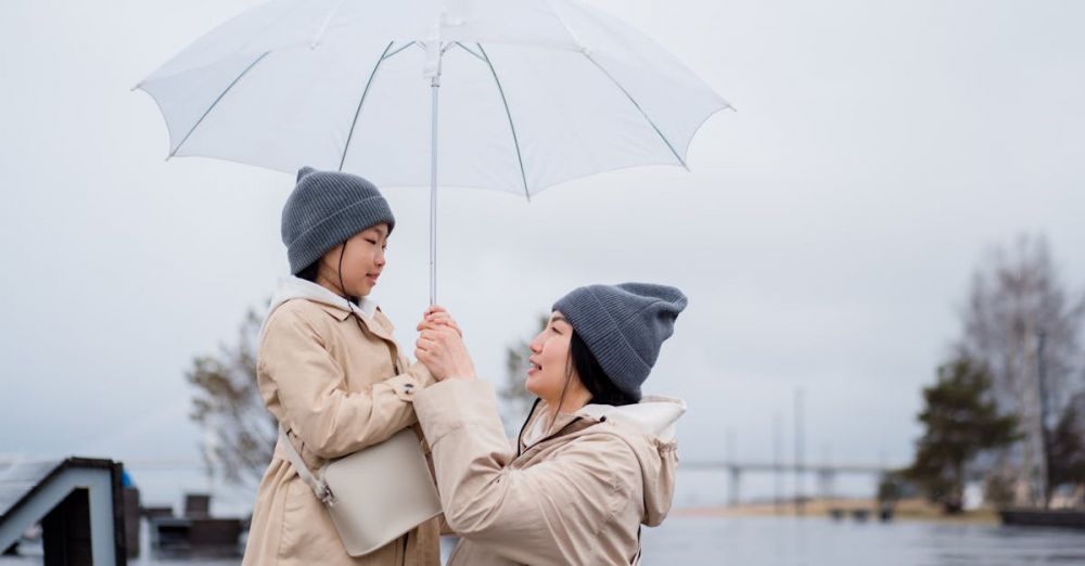 Waterproof Bags - Mother and daughter in matching coats and beanies holding an umbrella, enjoying a rainy day outdoors.