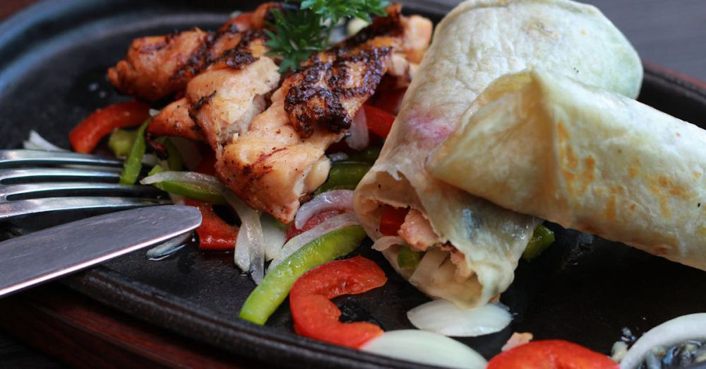 Wrap - Delicious grilled chicken with peppers and onion wrapped in soft flatbread on a sizzling plate.