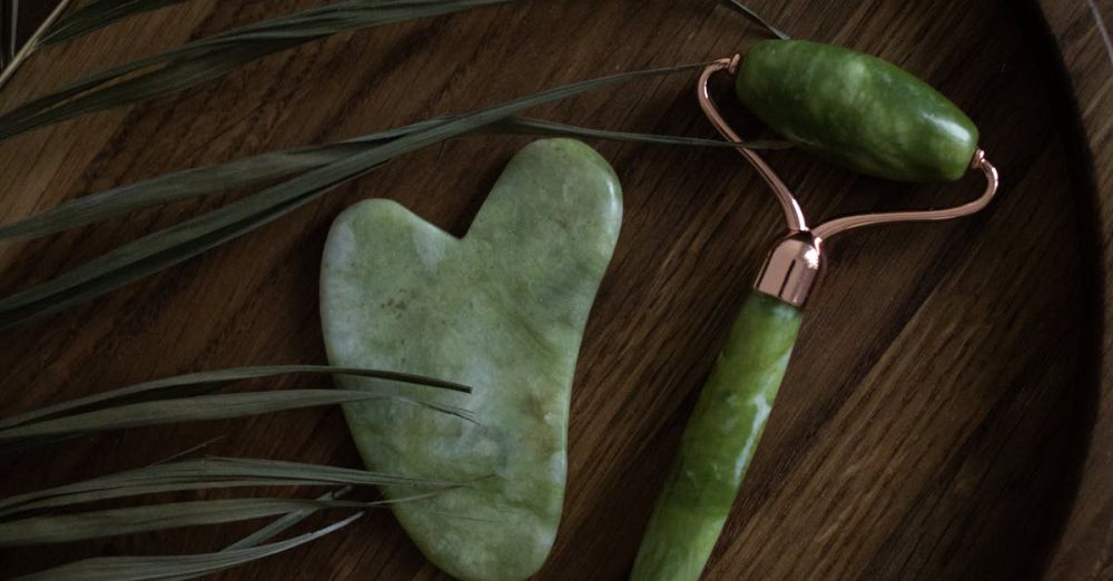 Anti-Aging Products - A jade roller and gua sha stone on a wooden tray with green leaves, perfect for skincare routines.