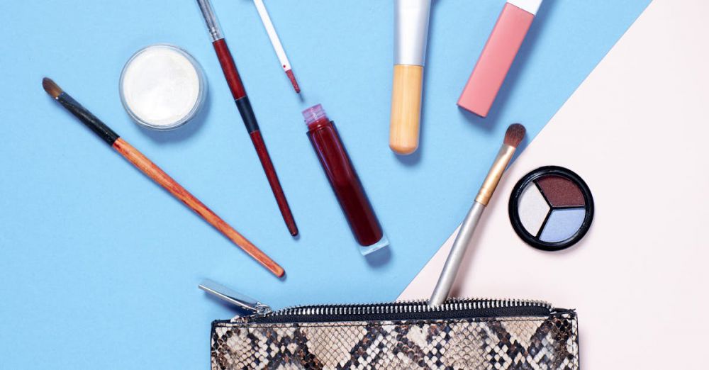 Beauty Products - A flat lay of vibrant makeup items arranged around a stylish snakeskin cosmetic bag on a blue and beige background.