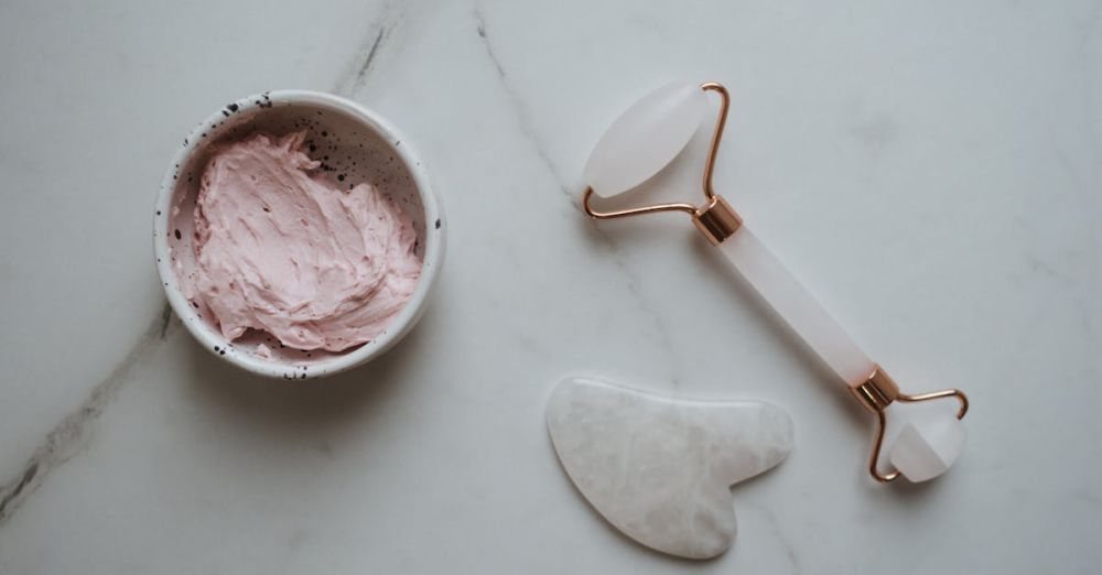 Facial Tools - Top view of gua sha tools and pink facial cream on a marble countertop.