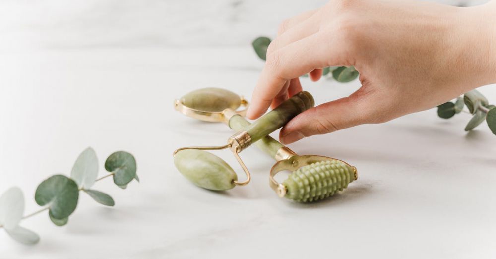 Face Rollers - Close-up of a hand holding jade rollers on a marble surface for skincare and wellness.