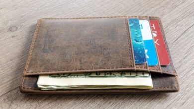 Wallets - A brown leather wallet with cash and credit cards on a wooden surface.