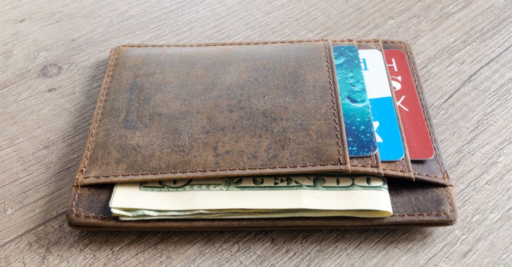 Wallets - A brown leather wallet with cash and credit cards on a wooden surface.