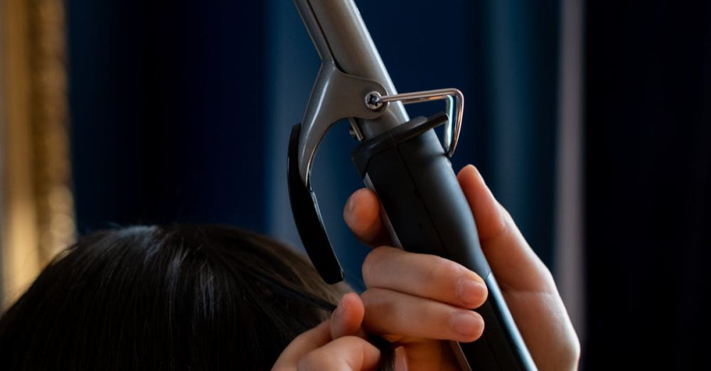 Curl Enhancers - Close-up of hands styling long brown hair with a curling iron in a salon.