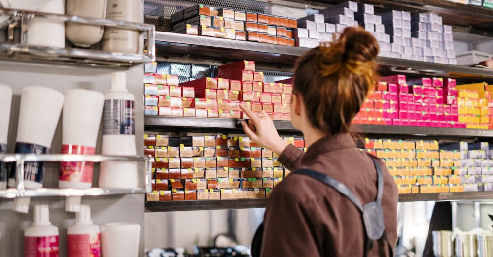 Hair Repair Products - A hairstylist organizing vibrant hair color boxes on a shelf in a beauty salon.