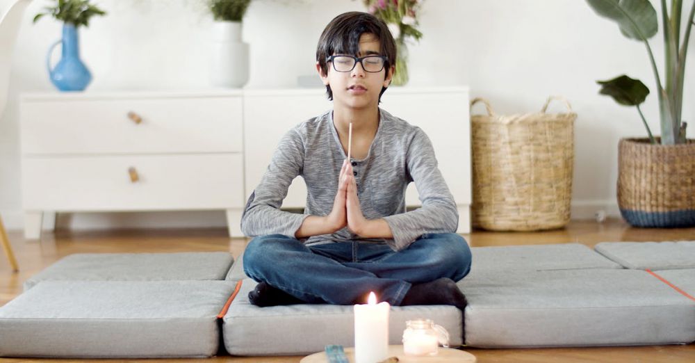 Meditation Cushions - Young boy meditating at home with eyes closed, surrounded by candles and plants.