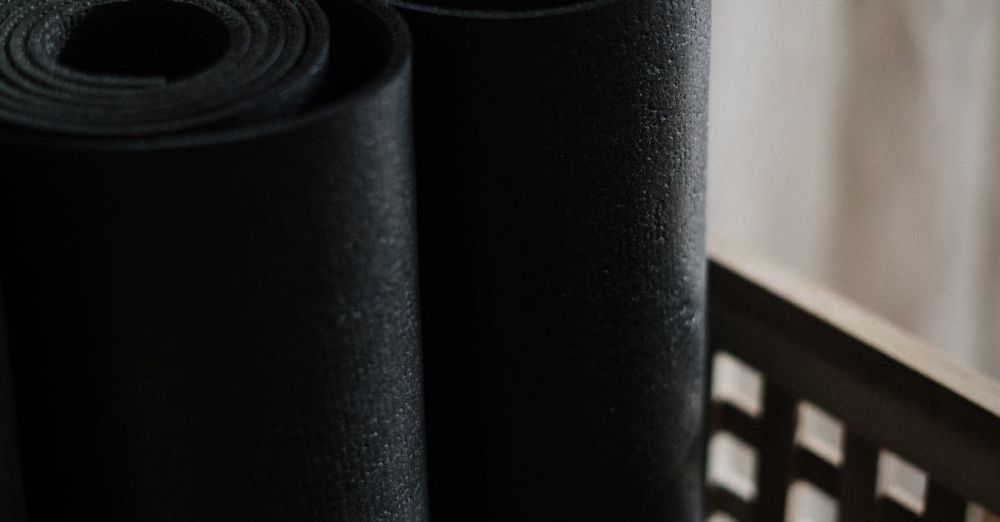 Yoga Mats - Close-up view of black yoga mats rolled and stacked in a wooden basket indoors.