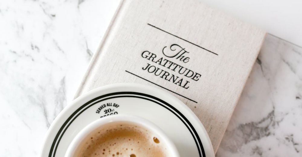 Gratitude Journals - A cup of coffee rests on a gratitude journal against a marble backdrop, capturing peaceful moments.