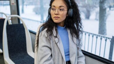 Music Playlists - Stylish woman in gray coat enjoying music through wireless headphones on a snowy day.