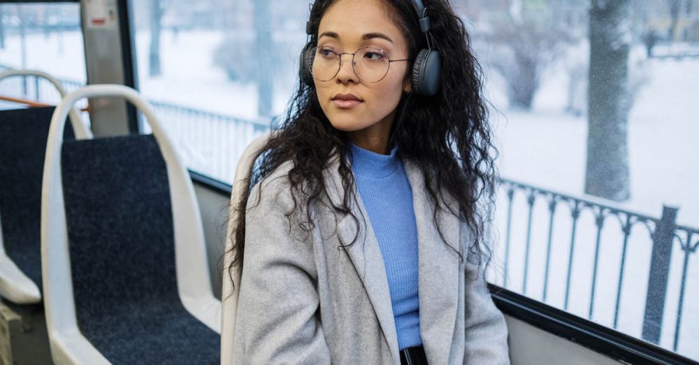 Music Playlists - Stylish woman in gray coat enjoying music through wireless headphones on a snowy day.