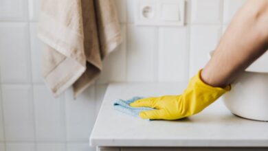 Bathroom Cleaners - Close-up of a person wearing yellow gloves wiping a bathroom counter with a cloth.