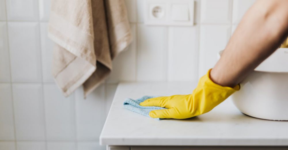 Bathroom Cleaners - Close-up of a person wearing yellow gloves wiping a bathroom counter with a cloth.