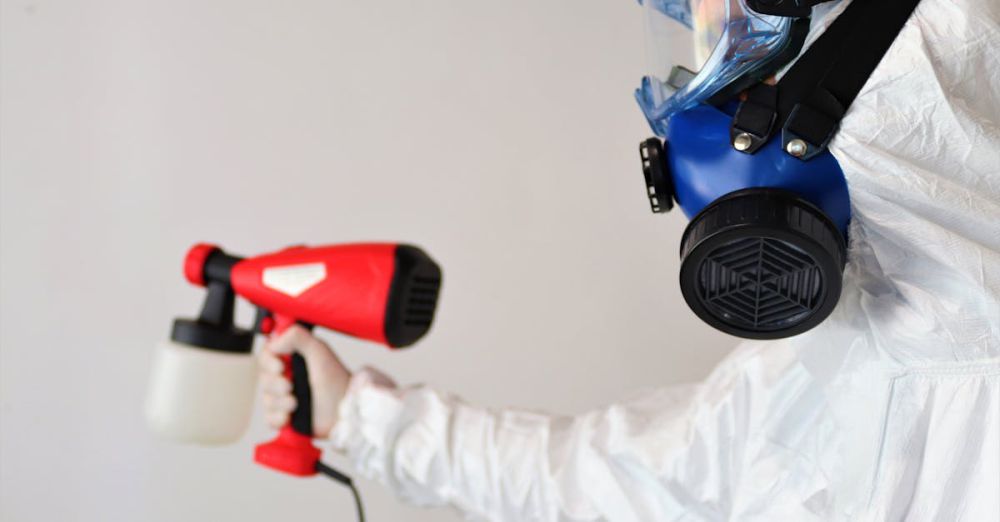 Mold Removers - A worker in protective gear uses a disinfectant spray indoors.