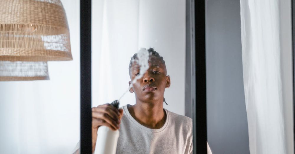 Cleaning Sprays - A young man uses a spray bottle to clean a glass window inside a modern room.