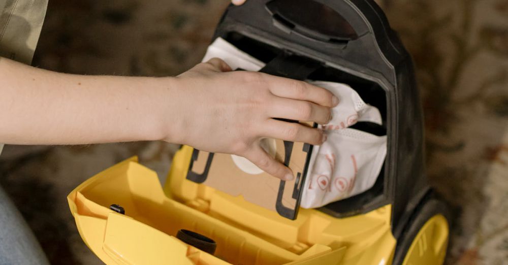 Vacuum Accessories - Individual replacing a bag in a yellow vacuum cleaner on a patterned carpet.