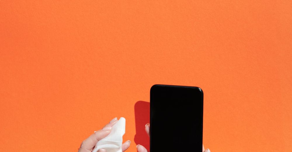 Disinfectant Wipes - Hands cleaning a smartphone with wipes against a vibrant orange background, emphasizing hygiene.