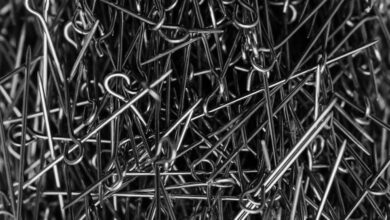 Steel Products - A high-contrast black and white image of metallic sewing pins in a cluttered pile.