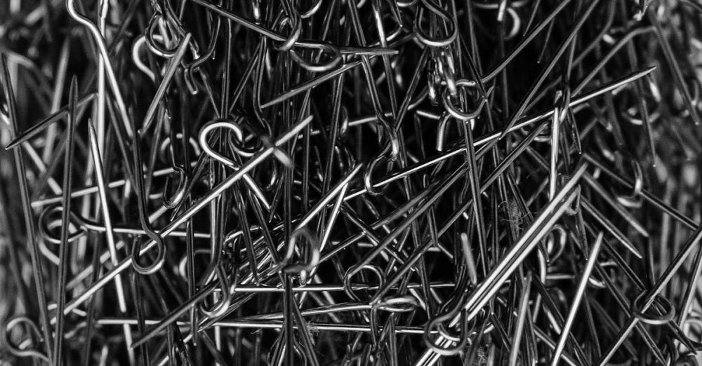 Steel Products - A high-contrast black and white image of metallic sewing pins in a cluttered pile.