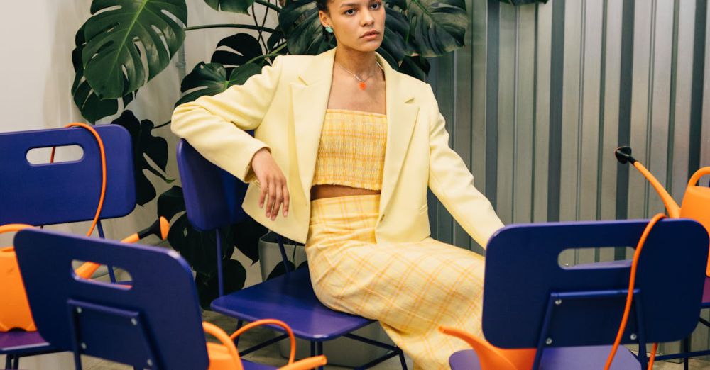 Watering Cans - Stylish woman in a yellow blazer sitting among purple chairs and green monstera plants indoors.