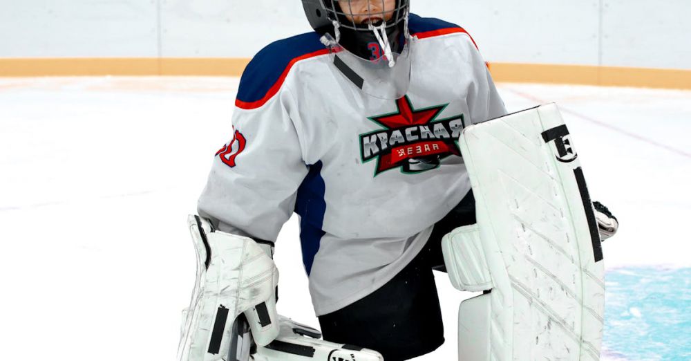 Kneeling Pads - Goalkeeper in full gear kneeling on ice hockey rink indoors.