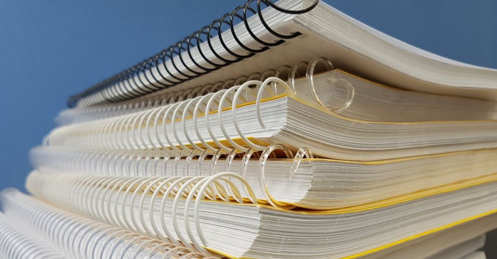 Notebooks - Close-up of stacked spiral notebooks with varied bindings against a blue backdrop.