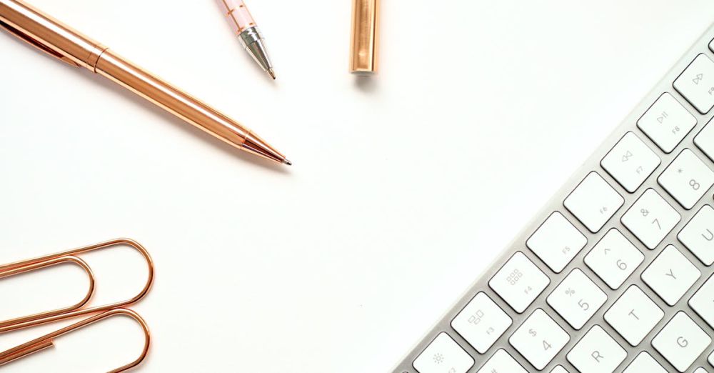 Pens - Elegant minimalist workspace featuring rose gold pens, paper clips, and a sleek keyboard for a stylish office setup.