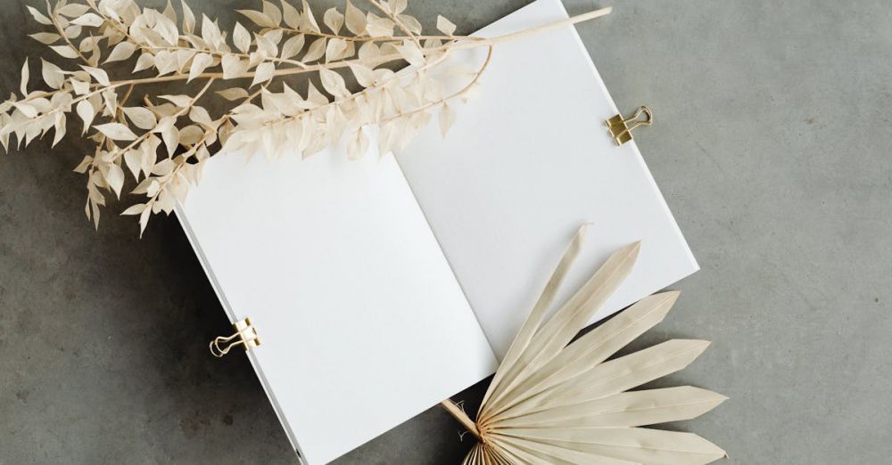 Paper Products - A minimalist flat lay featuring a blank notebook and dry botanical leaves on a concrete surface.