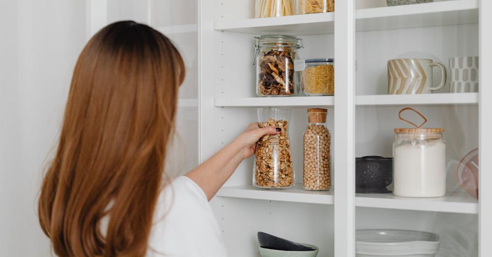 Storage Solutions - Woman arranging jars on pantry shelves for organized food storage.