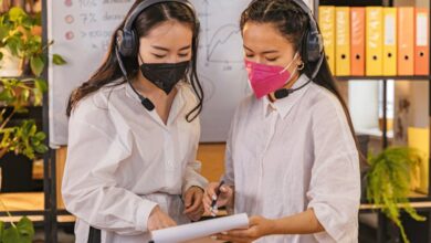 Whiteboards - Two women in a modern office reviewing documents while wearing masks and headsets.