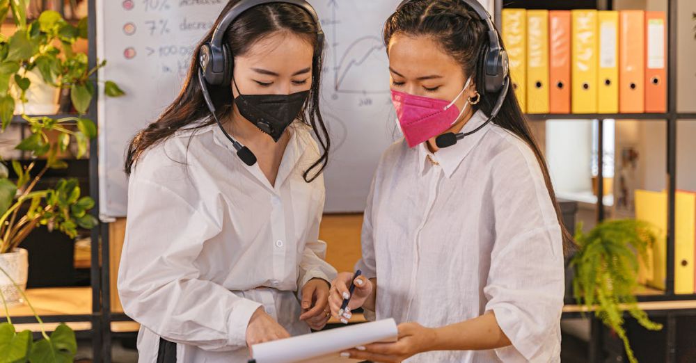 Whiteboards - Two women in a modern office reviewing documents while wearing masks and headsets.