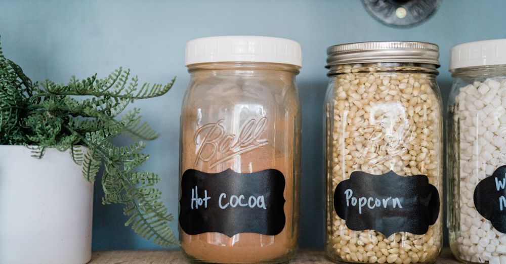 Kitchen Organizers - Glass jars with popcorn, hot cocoa, and marshmallows on a kitchen shelf with a potted plant.