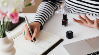 Jewelry Organizers - Unrecognizable female using pen and writing notes in notepad while sitting at table and waiting when polish nail getting dry