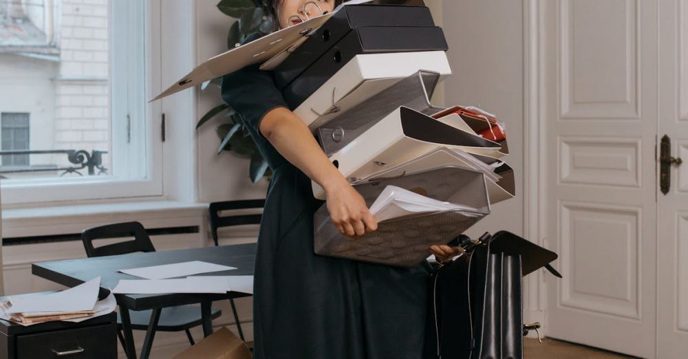 File Boxes - Asian woman in a black dress struggling to hold multiple document boxes in an office setting.