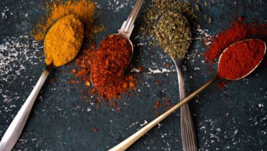 Spice Racks - Top view of vibrant spices in spoons on a textured dark surface.