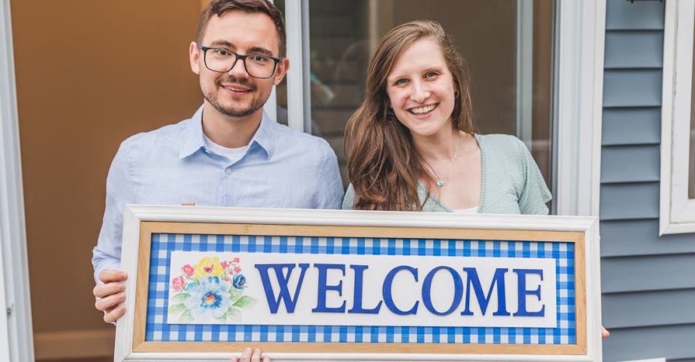 Key Holders - A cheerful couple stands at their new home entrance holding a welcome sign.