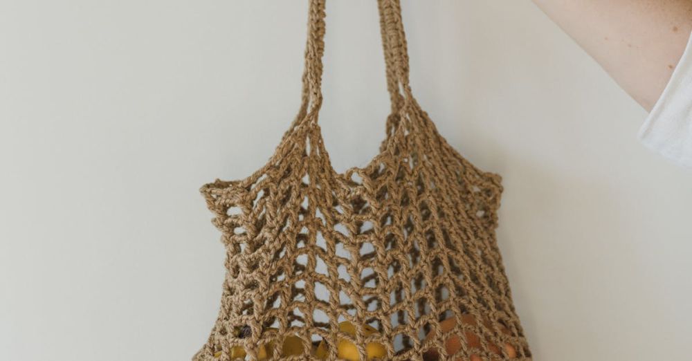 Holders - A hand holding a crocheted bag filled with yellow fruits against a plain background.