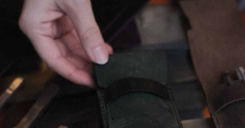 Passport Products - Close-up of a hand holding a green leather wallet on a display table with other leather items.